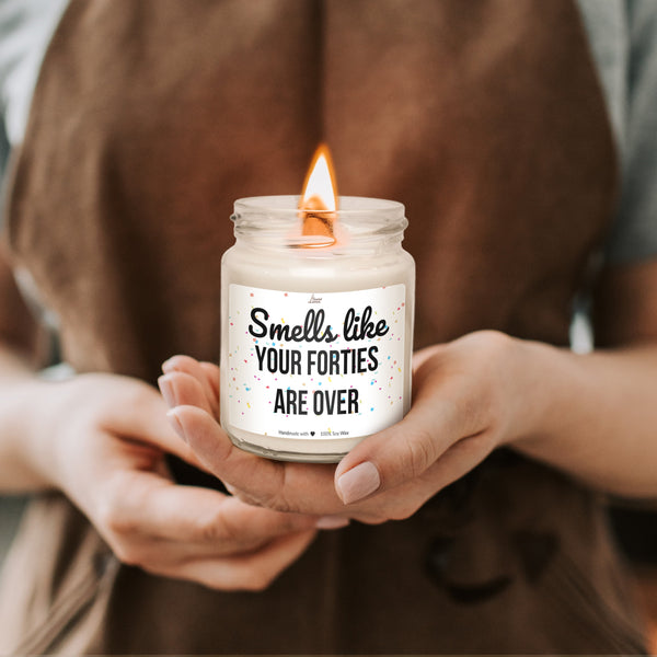 a woman holding a candle that says smell like your forties are over