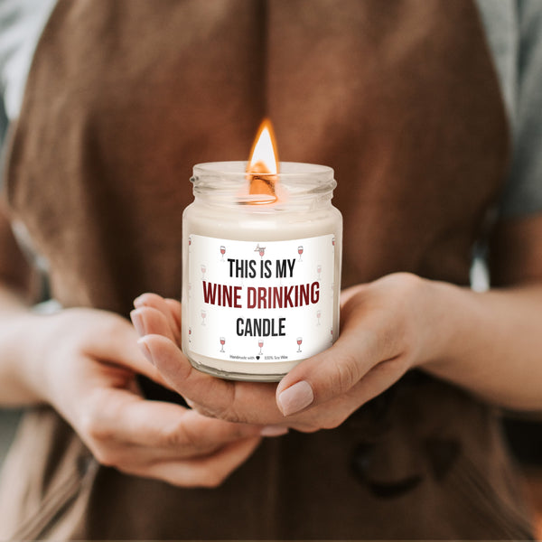 a woman holding a candle that says, this is my wine drinking candle