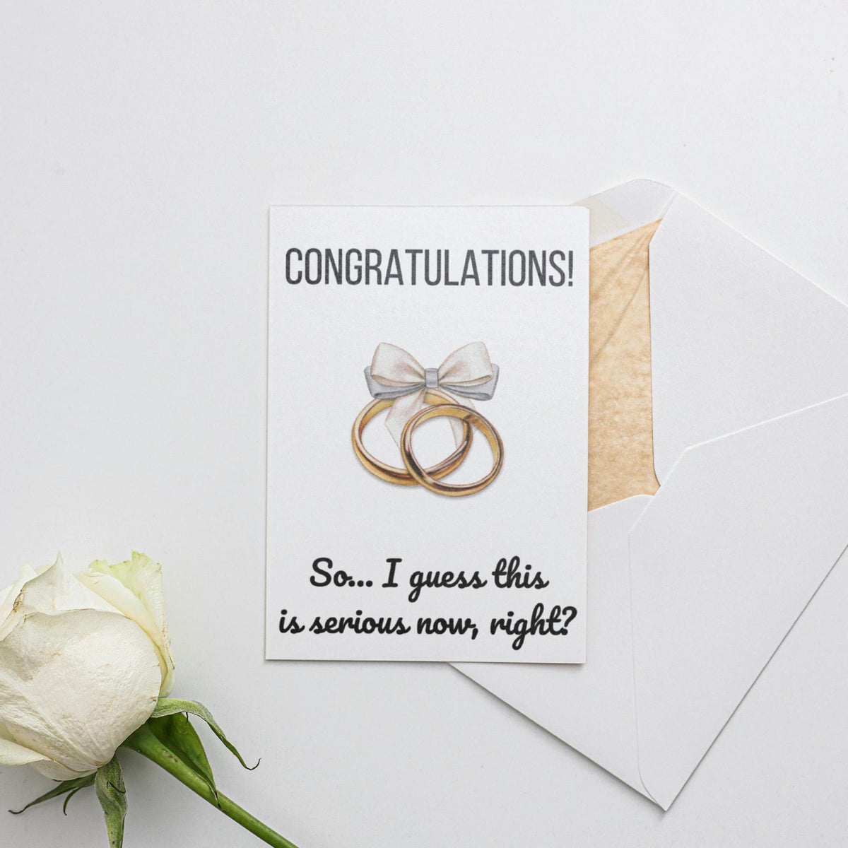 a white rose and two wedding rings on a card