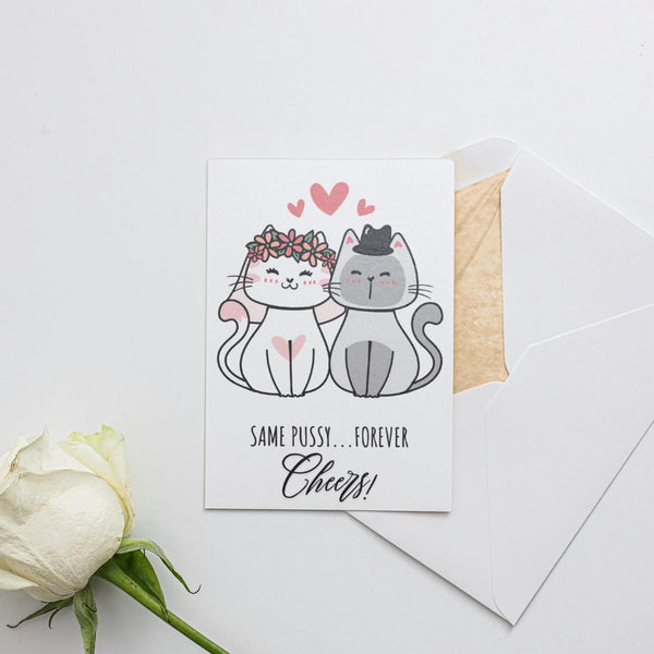 a white rose sitting next to a card with two cats on it